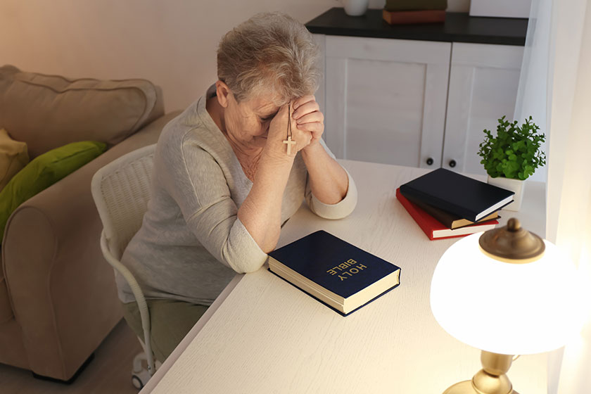 Religious elderly woman praying over Bible at table