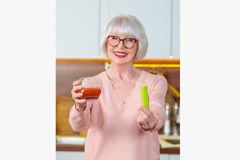 Senior cheerful woman with celery and tomato juice diet kitchen raw