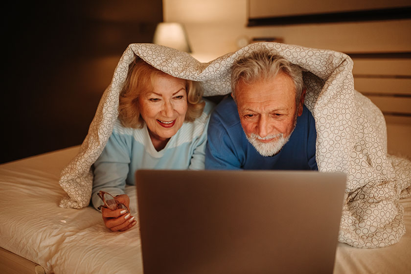 Lovely senior couple using laptop while lying on bed