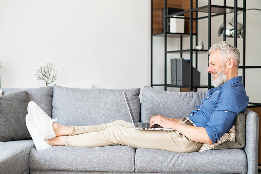 Optimistic middle-aged man lying on the couch and using laptop