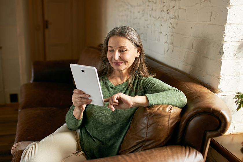 Beautiful woman pensioner relaxing on comfortable leather sofa with digital tablet