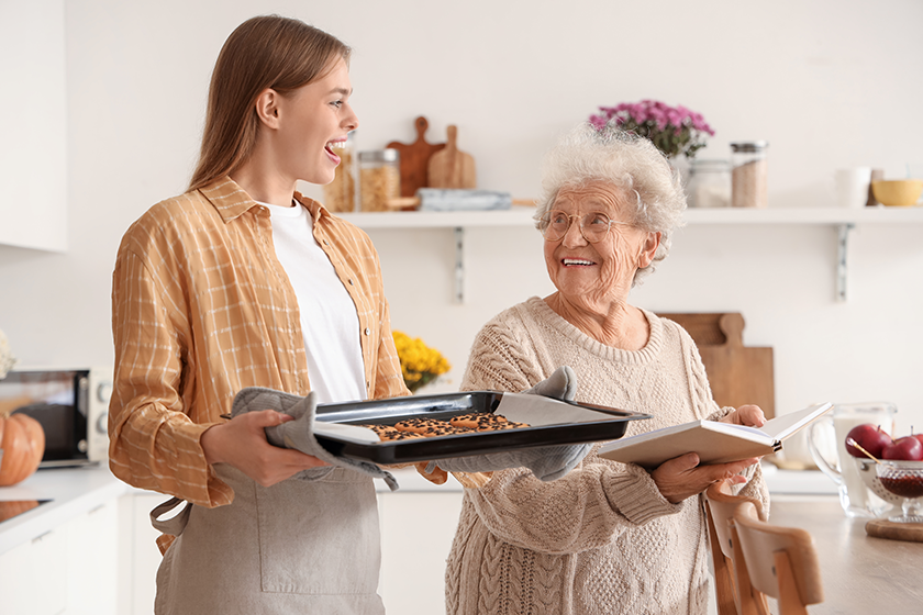 Young woman holding baking tray with cookies and her grandmother in kitchen